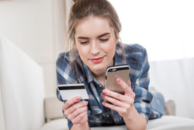 A woman making a payment on her phone in one hand while holding her credit card in the other.