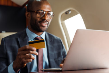 A businessman using his computer while holding his credit card in his hand.