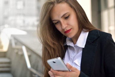 A person in business attire checks their phone on some stairs in a city.